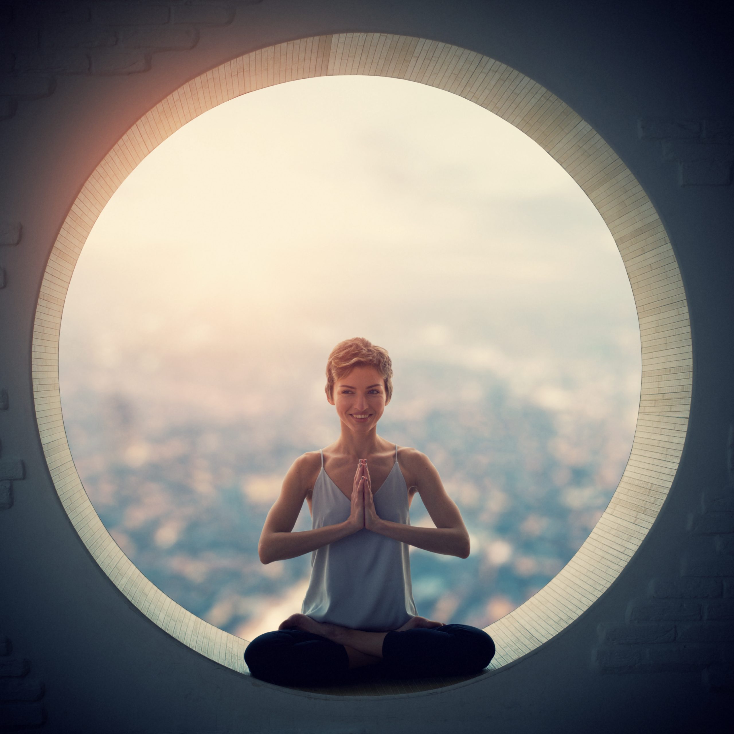 Beautiful sporty fit yogi woman practices yoga asana Padmasana - Lotus pose in a round window