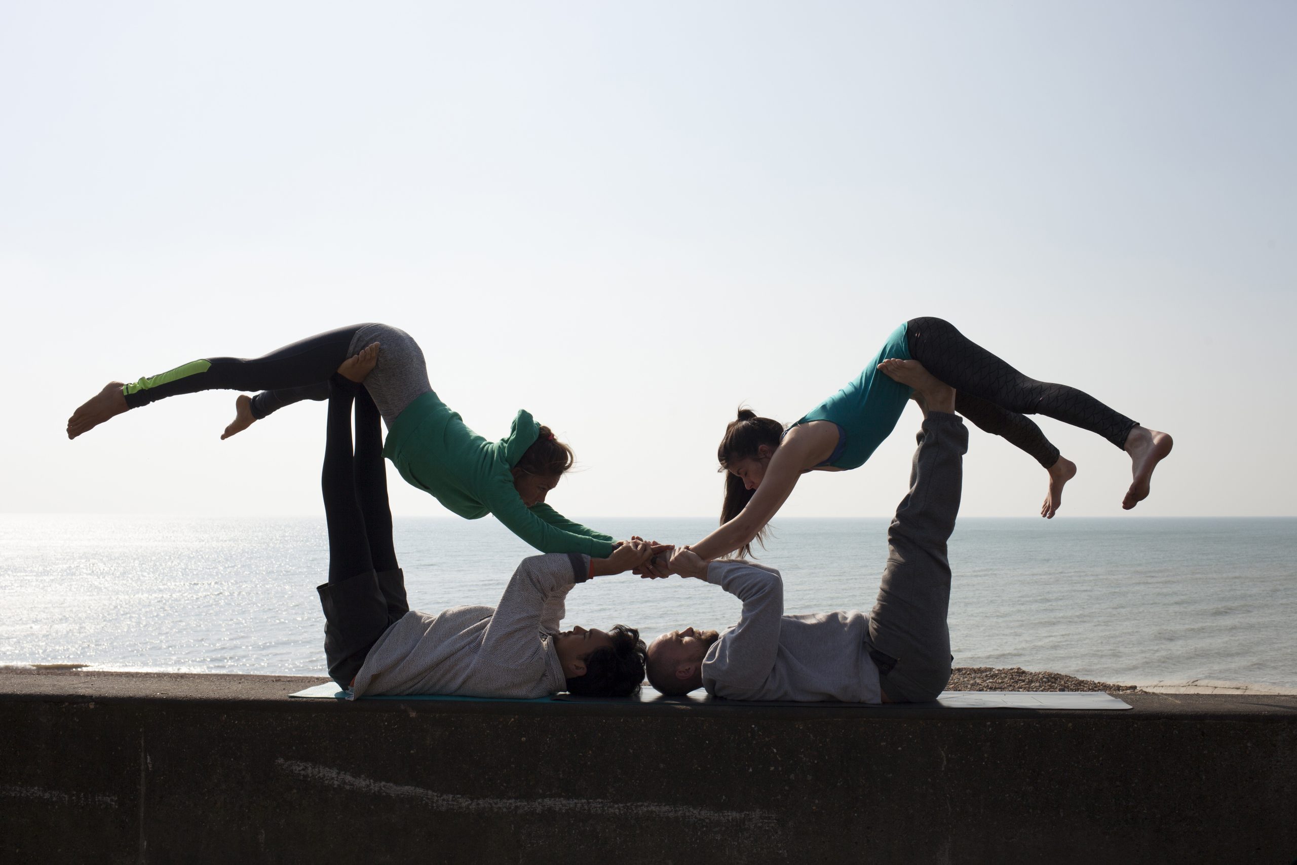 Silhouetted men and women practicing acrobatic yoga on wall at Brighton beach